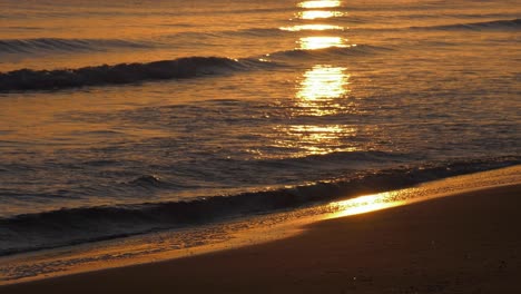 Olas-Doradas-Que-Reflejan-La-Salida-Del-Sol-Suavemente-Lamiendo-En-La-Playa-De-Arena,-Playa-Tropical-Paradisíaca,-Costa-Temprano-En-La-Mañana