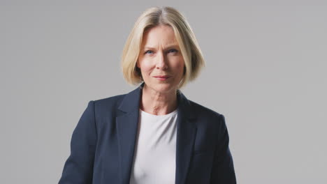 Studio-Portrait-Of-Mature-Businesswoman-With-Serious-Expression-Standing-Against-Plain-Background