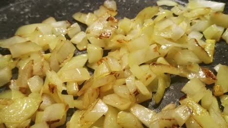 close up moving over white onions frying in a pan releasing steam as they slowly turn gold and brown