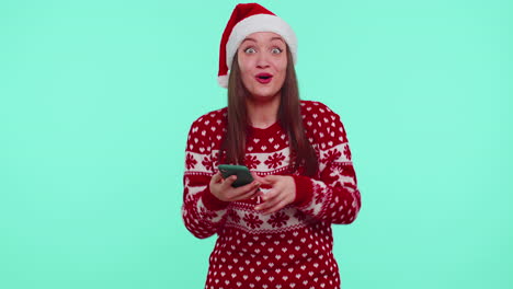 Young-teen-girl-in-Christmas-sweater-looking-smartphone-display-sincerely-rejoicing-win-success-luck