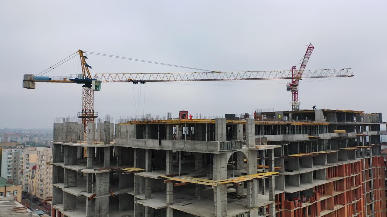 Process of construction high-rise building. Labor workers on a big construction site on the background of working crane in the city. Slow motion. Camera moves top down.