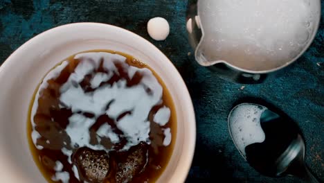 vista superior del café que se vierte en una taza blanca con burbujas circulares en una mesa cambiante y vibrante