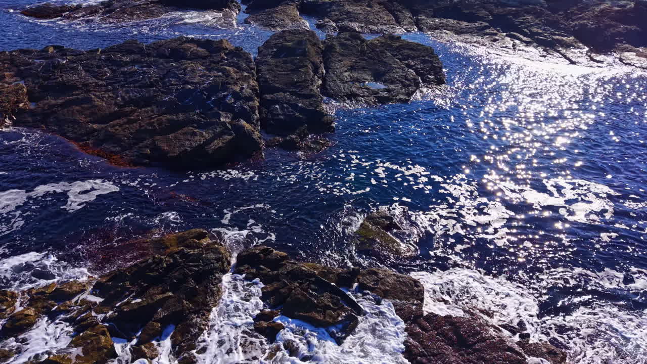 Waves crashing over rocky shoreline under sunny skies, capturing the beauty of nature in vibrant blue hues