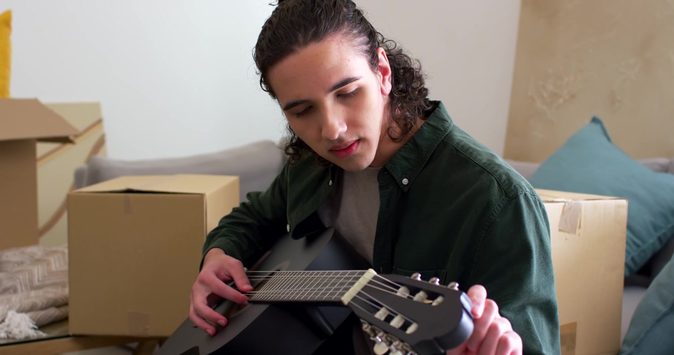 Hombre afroamericano en un sofá afinando una guitarra después de pulsar una cuerda, comprobando el tono moviendo cajas.