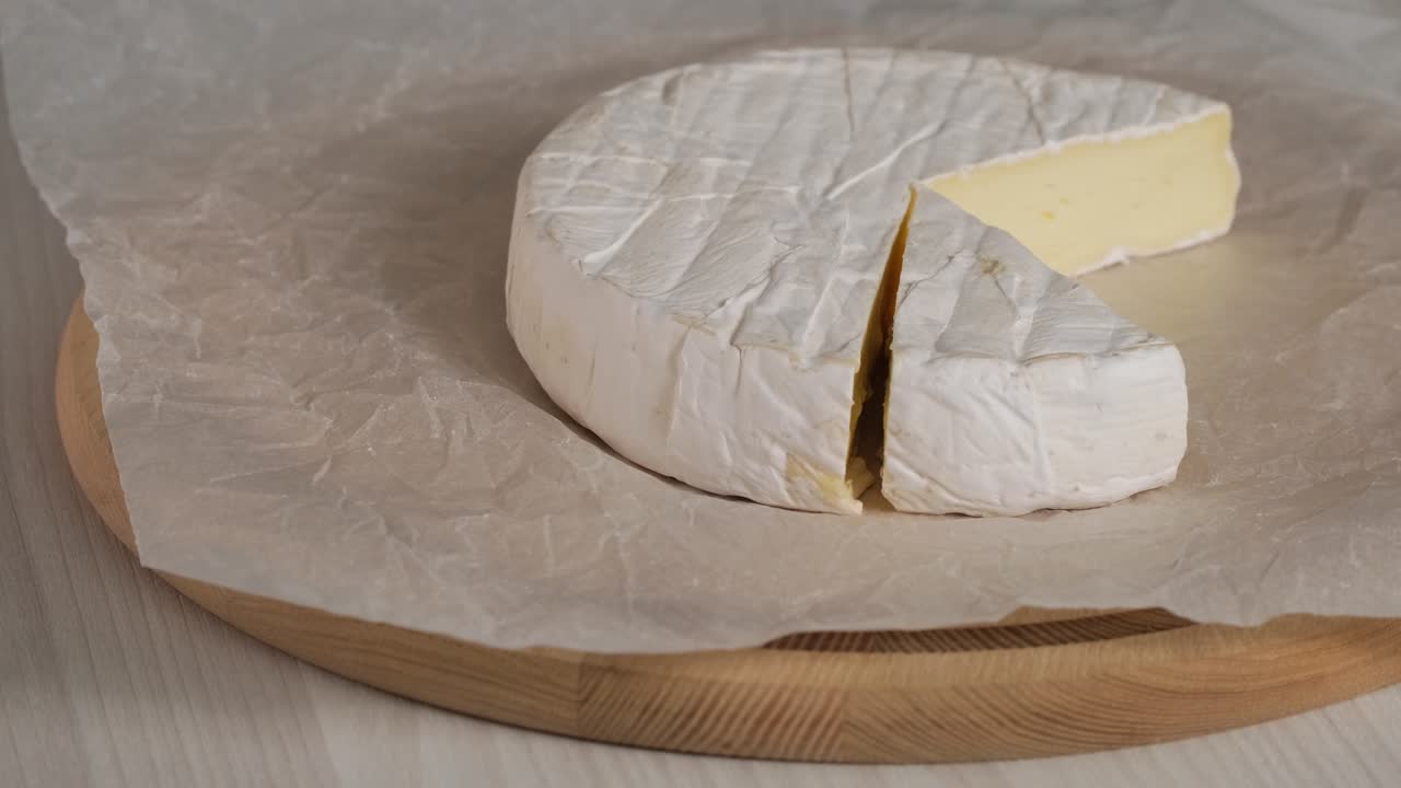 queso crema camembert de primer plano giratorio. cabeza de queso de leche de cabra con moho blanco en tabla de madera. cabeza redonda camembert cortado en pedazos delicioso queso suave camembert