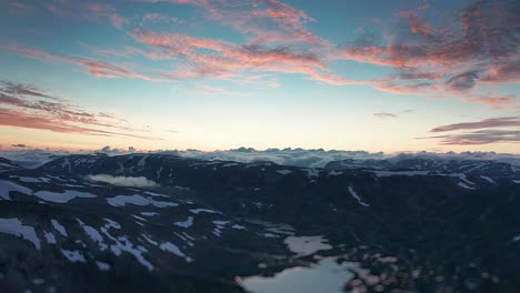 Vuelo-Sobre-El-Valle-De-Strynefjellet-Con-Nubes-Rosadas-Al-Atardecer-Sobre-La-Meseta-Rocosa-Con-Lagos-Y-Parches-De-Nieve