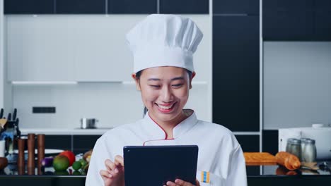 mujer chef apuntando a la tableta en la cocina