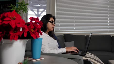 Mujer-Joven-Hispana,-Trabajando-En-Casa-En-Una-Computadora-Portátil-Durante-El-Día-De-Trabajo,-Moviéndose-Lentamente-Pasando-La-Planta