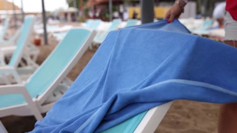 person spreading a blue towel on a beach lounge chair