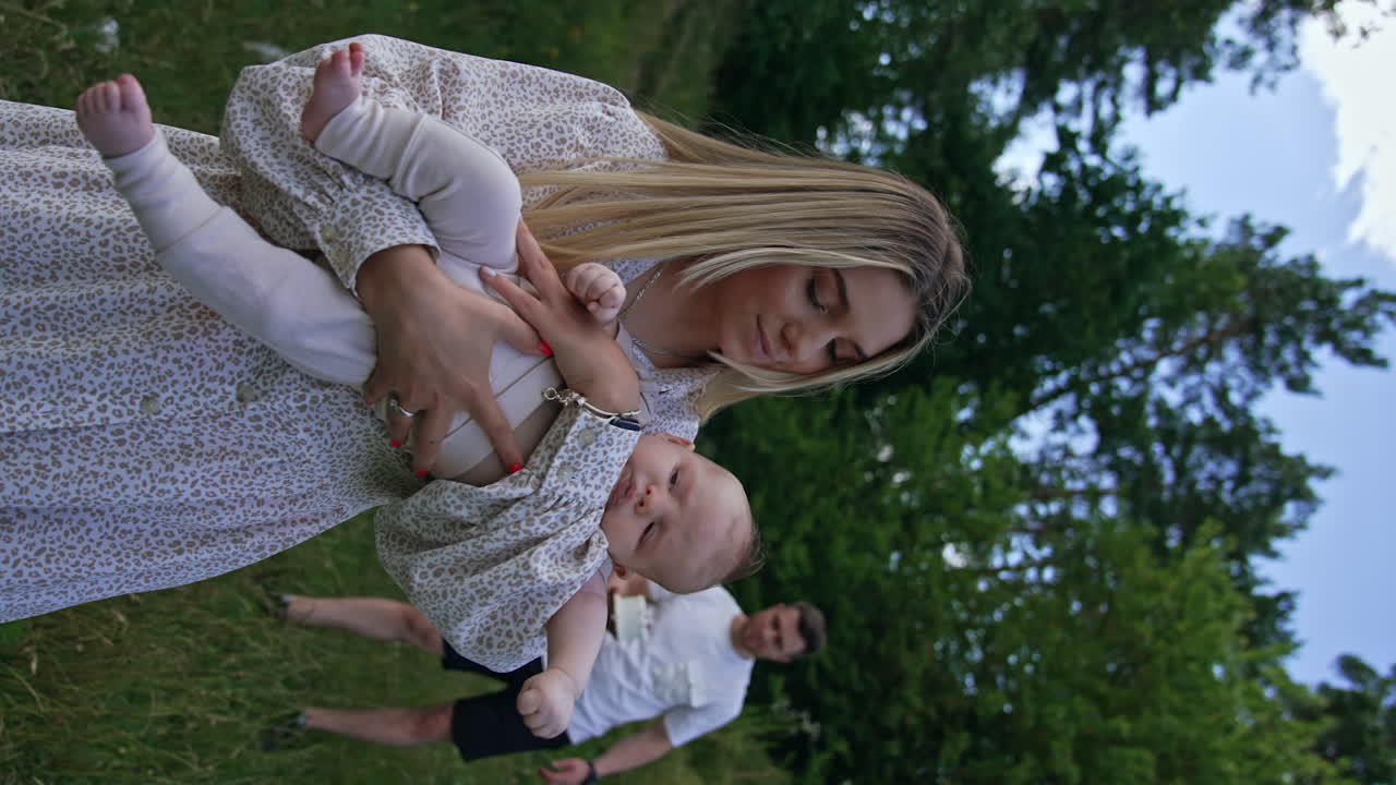 Blonde beautiful woman waving her newborn in hands. Her husband comes up bringing a cake on the plate. Vertical screen.