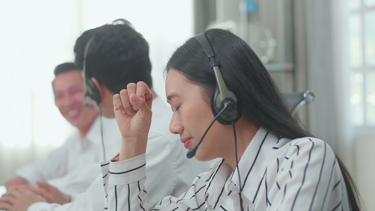 A Woman Of Three Asian Call Center Agents Wearing Headset Is Tired Because Two Of Her Colleagues Are Talking During Working At The Office