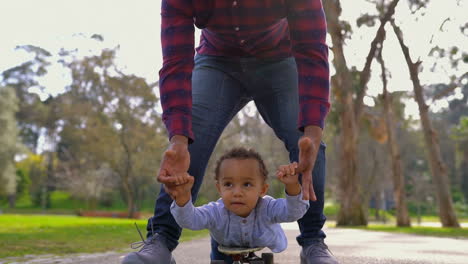 niño acostado en patineta, rodando hacia la cámara con la ayuda de su padre