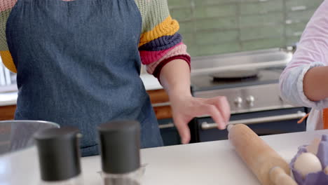 Happy-biracial-mother-and-daughter-baking-in-sunny-kitchen