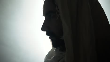 closeup of the face of jesus christ resurrected on easter sunday inside empty tomb in bright, shining light, wearing white hood and robe. cinematic christian visual.