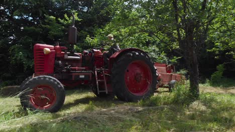 tracking shot of a farmer driving a hay baler among trees on a field