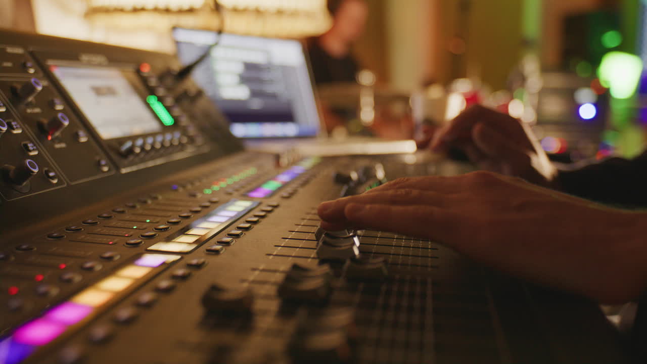 Audio engineer adjusting knobs on professional mixing console in a cozy music studio with warm light