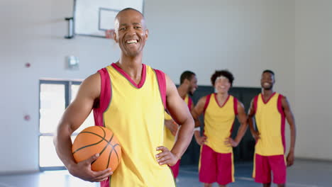 hombre afroamericano sostiene una pelota de baloncesto en un gimnasio