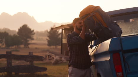 portrait of man unloading backpacks from pick up truck on road trip to cabin in countryside