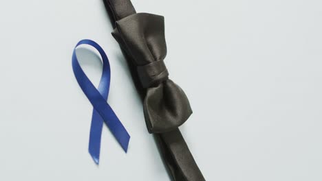 video of black bow tie and dark blue colon cancer ribbon on pale blue background