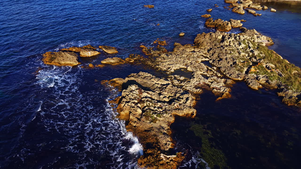 Majestic coastal rocks rise from vibrant blue waters under the warm sun, showcasing nature's beauty and tranquility at the shoreline