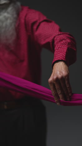 vertical video low key studio lighting shot of senior sikh man folding fabric for turban against plain dark background