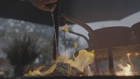 pouring alcohol over some meat that's cooking on a barbeque