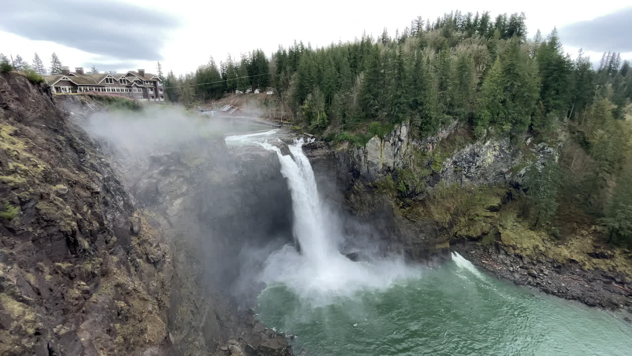amplia toma de agua que cae sobre las cataratas snoqualmie en el estado de washington, con niebla a su alrededor y el albergue en la parte superior