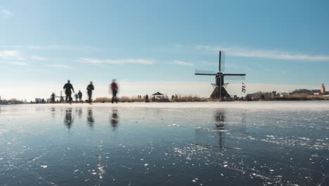 time lapse of dutch ice skaters on frozen canal beside old windmill, slider shot
