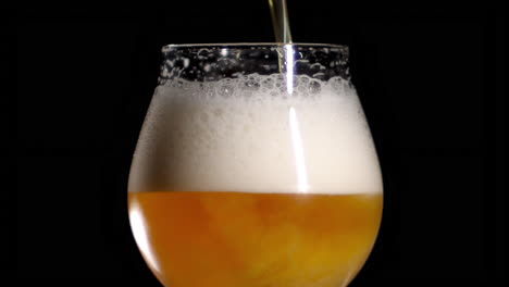 cierre en cámara lenta de la cerveza artesanal que se vierte en un vaso de tulipán, fondo negro