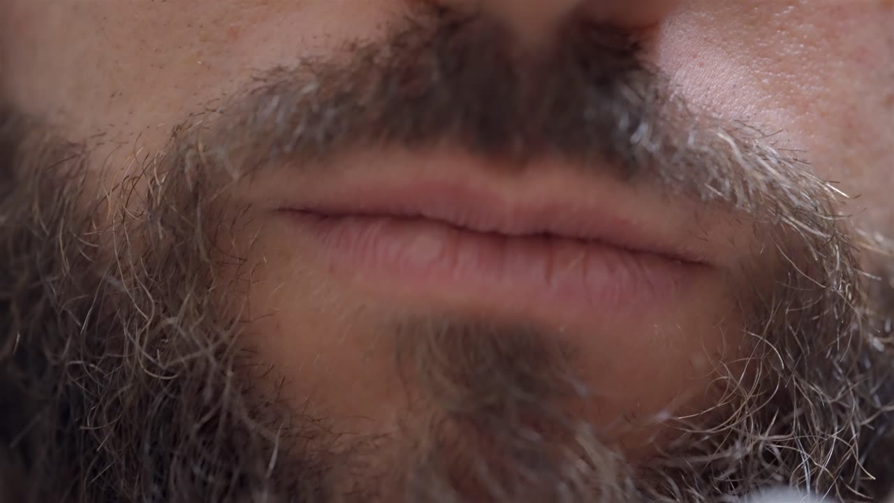 A close-up shot of a bearded man as he starts brushing his teeth with a toothbrush, focusing on the details.