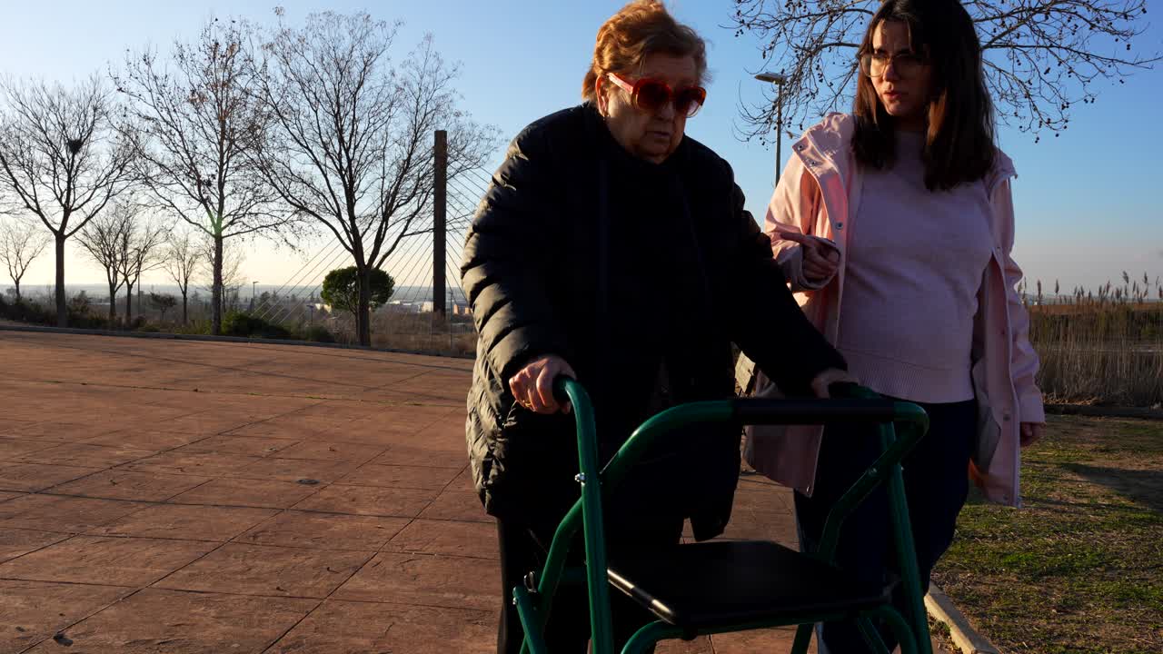 Old woman with a walker in the park accompanied by her pregnant granddaughter