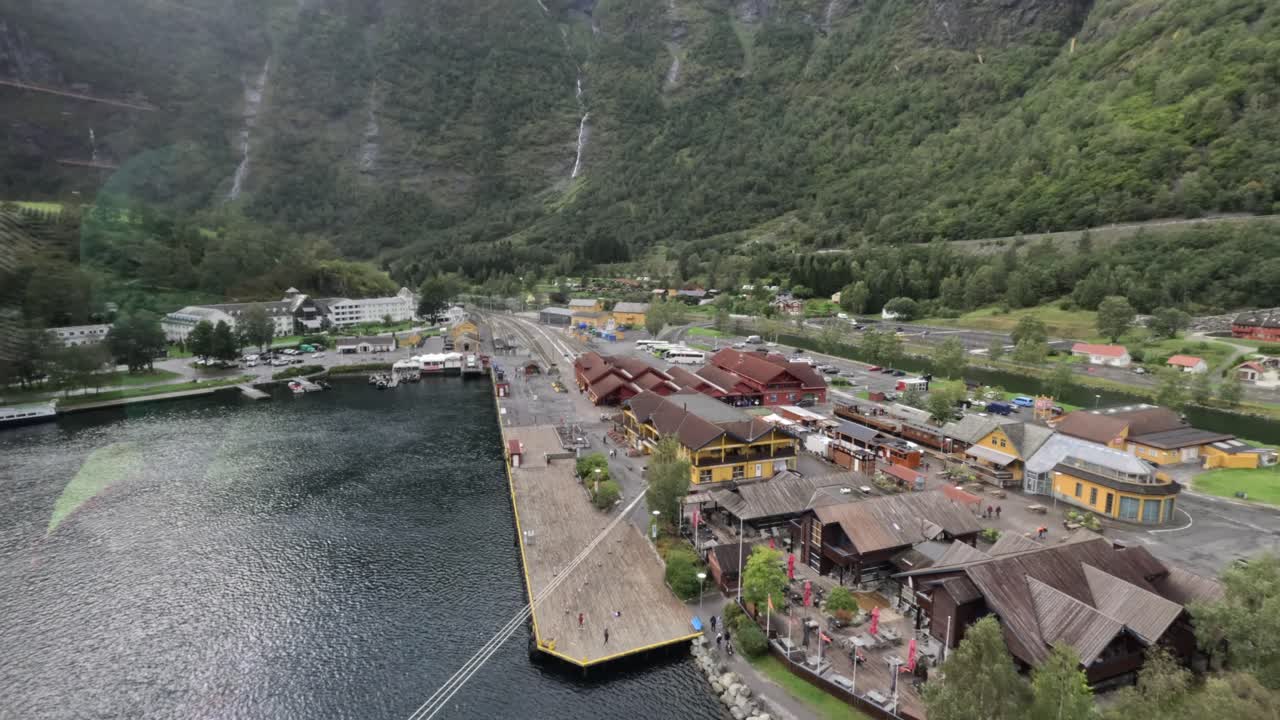 An ultra wide panning shot captures the village of Flåm in Vestland, Norway, revealing steep-roofed buildings, a cascading waterfall, and the serene fjord landscape in sweeping cinematic motion