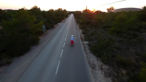 Disparo-De-Un-Dron-Siguiendo-Un-Scooter-En-Una-Carretera-Entre-árboles