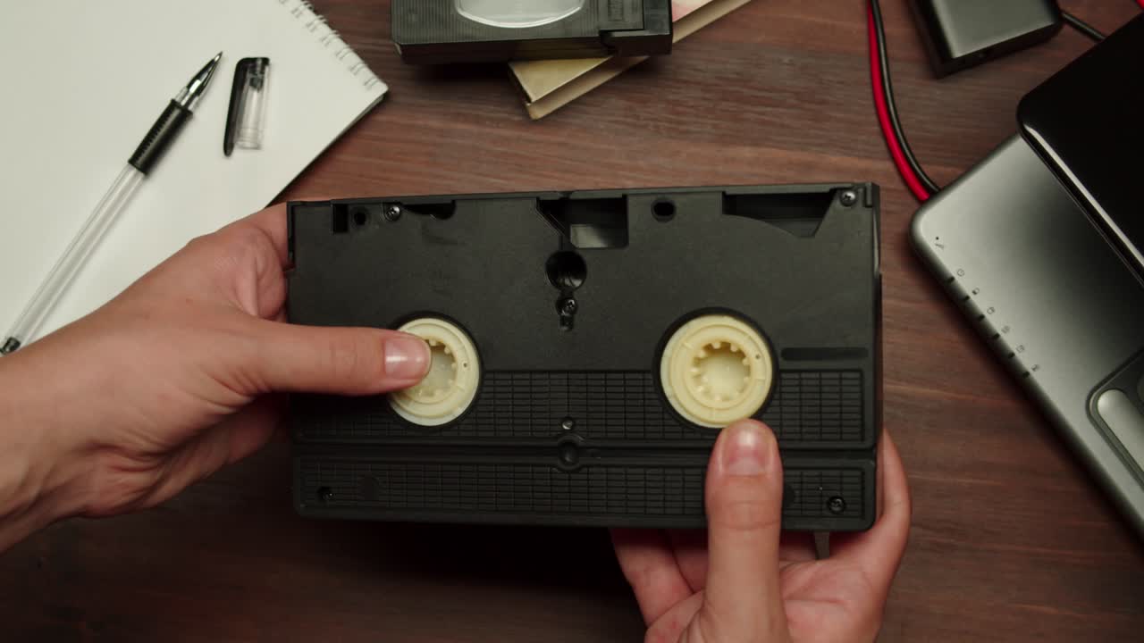 Hands Inspecting a Retro VHS Video Cassette on a Wooden Desk