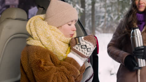 Teenager-Mädchen-In-Winterkleidung-Sitzt-Im-Kofferraum-Eines-Autos-Und-Trinkt-Heißes-Getränk