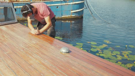 youth sanding boat cabin roof planks with sandpaper wearing mask