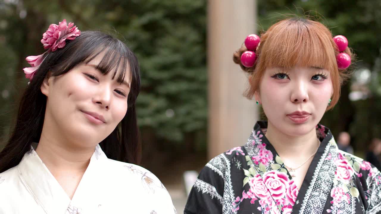 Due giovani donne che indossano kimono floreali sorridono e posano all'aperto presso un tradizionale santuario giapponese