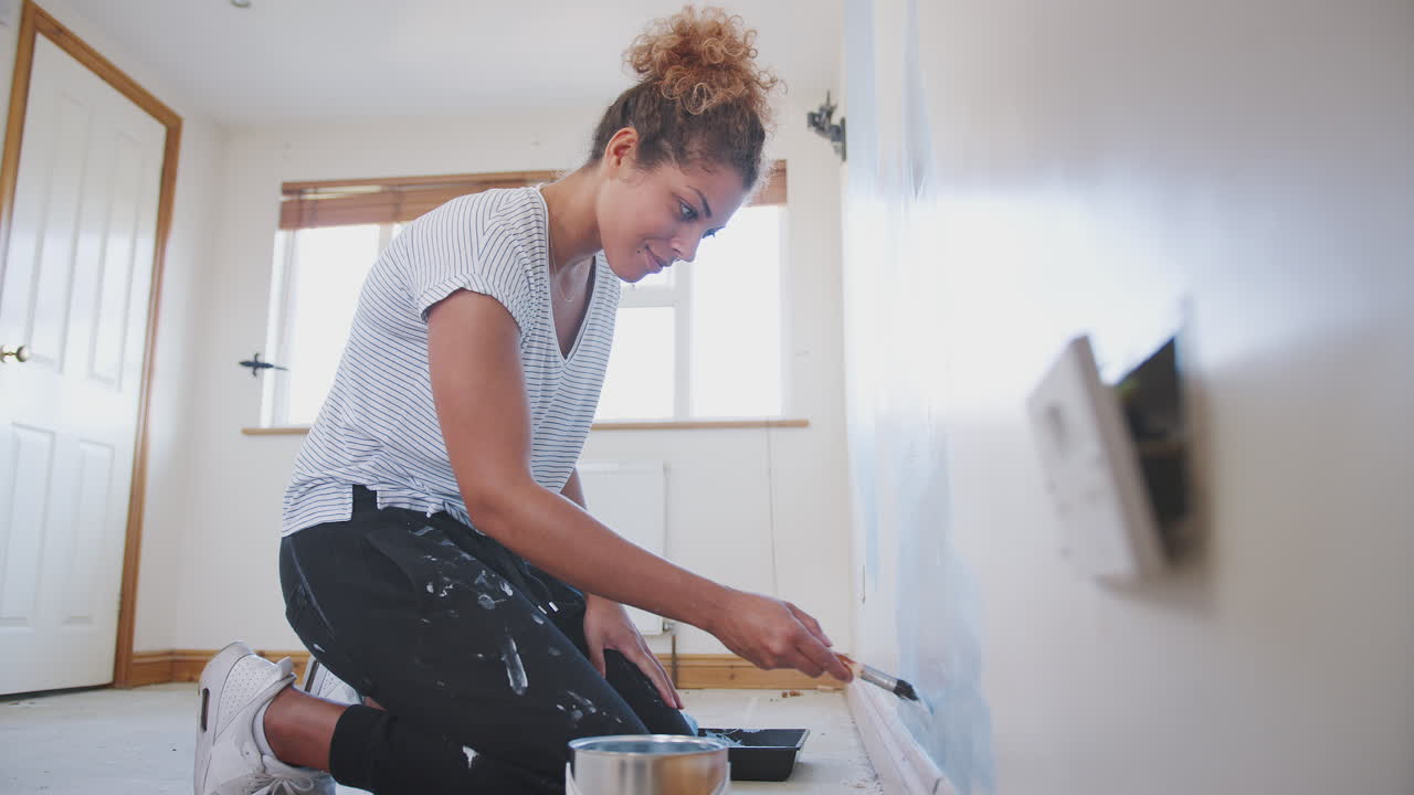 mujer joven decorando una habitación en una nueva casa pintando la pared con un pincel