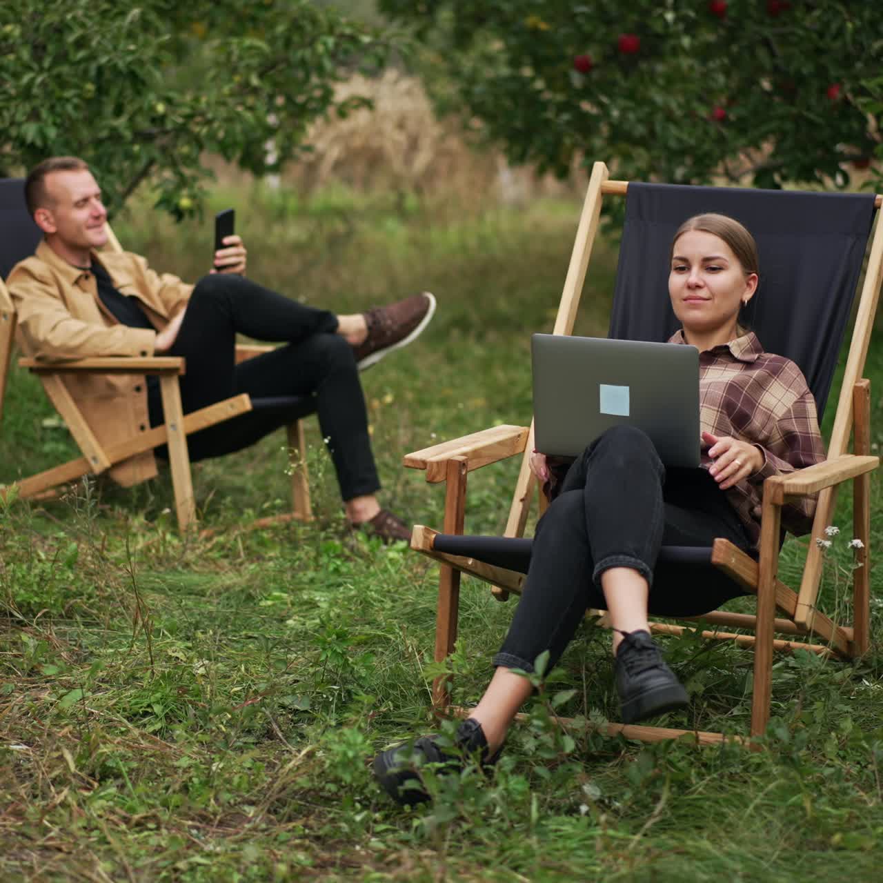 Chilling relaxed people working remotely on their laptops. Male and female sitting in the garden working as freelancers
