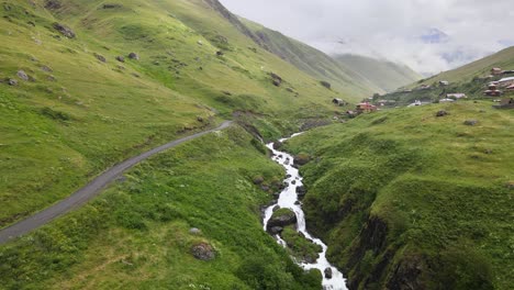 A-winding-road-runs-through-a-green-valley-with-a-stream-flowing-beside-it