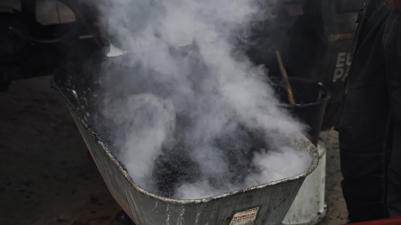 el betún o el asfalto caliente se cargan en una carretilla desde una máquina y un proceso de control de trabajadores de la construcción