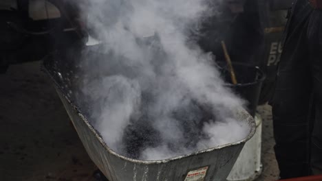 bitumen or hot asphalt is loaded into a wheelbarrow from a machine and construction worker controlling process