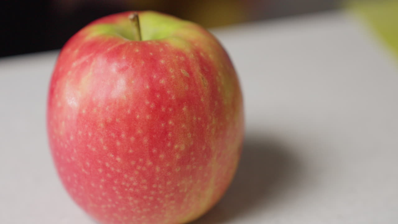 Close up red apple resting on white tissue as manicured hand reaches to pick it up, soft blur background detail on fruit surface, natural light highlights vibrant red peel and fresh texture