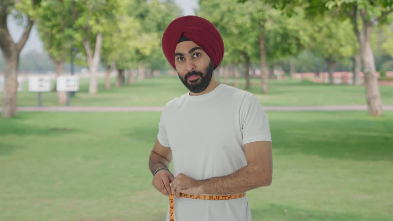 Uomo indiano Sikh felice che si misura la vita con un metro a nastro al parco