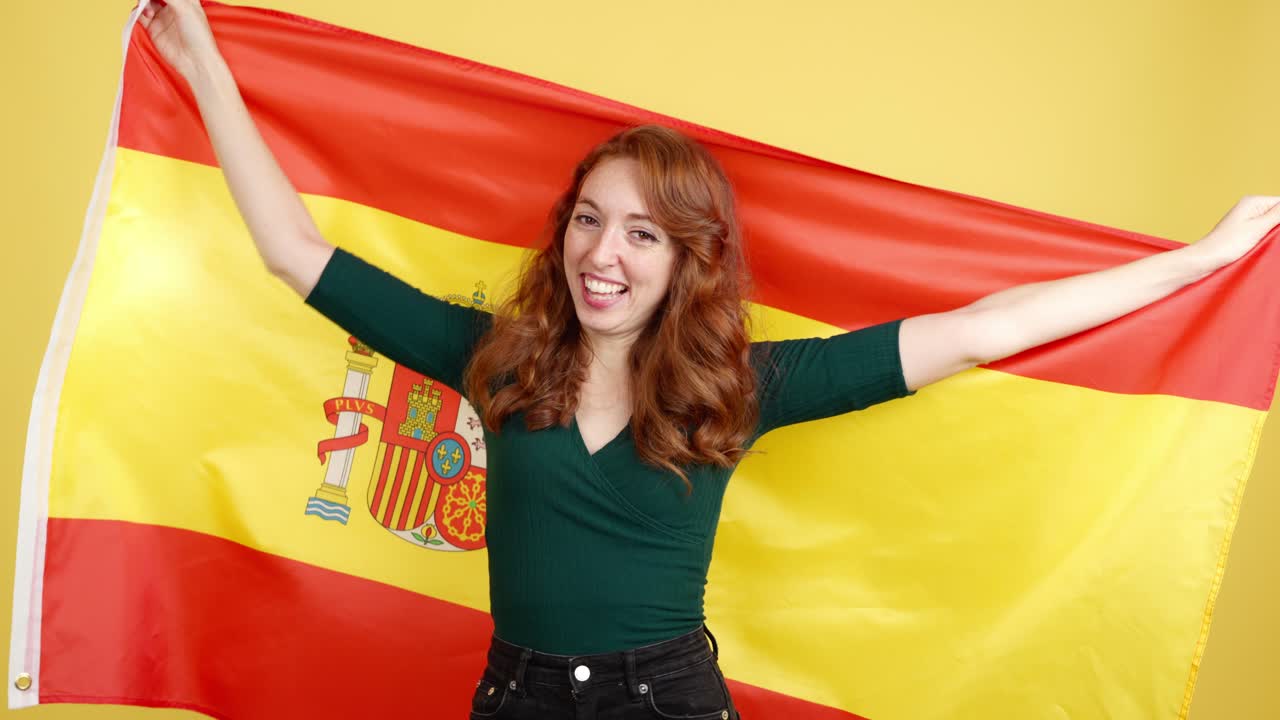 Happy woman wrapped in the Spanish flag on a yellow background