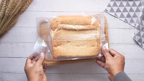 hands holding packaged sliced bread on wooden tray