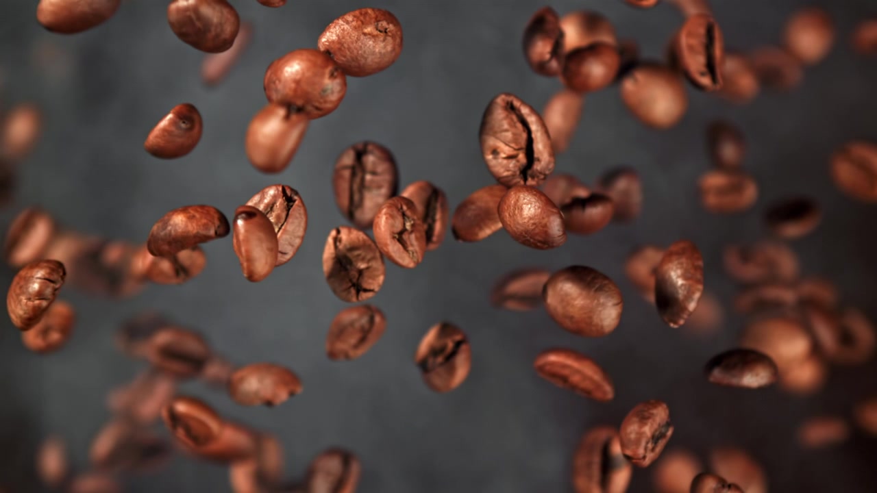 Chicchi di caffè tostati che cadono in super rallentatore con fumo.