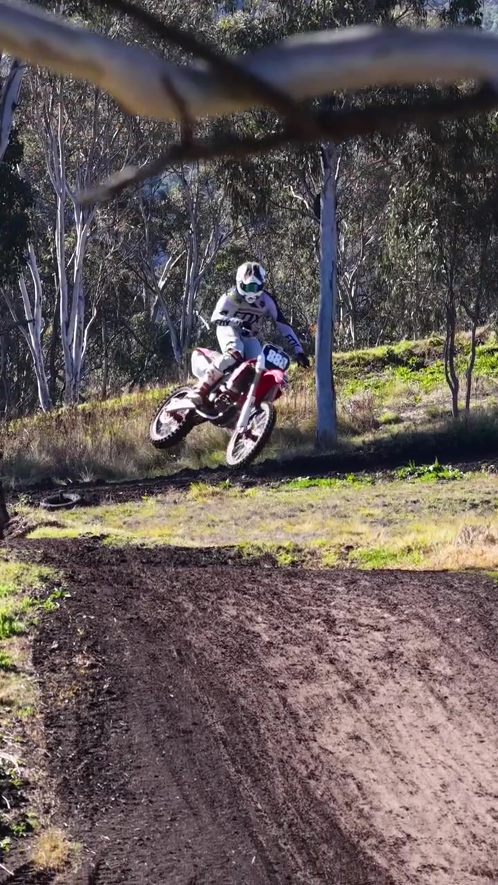 Foto vertical cheia de ação de pilotos de motocross saltando e correndo em uma pista de terra ensolarada