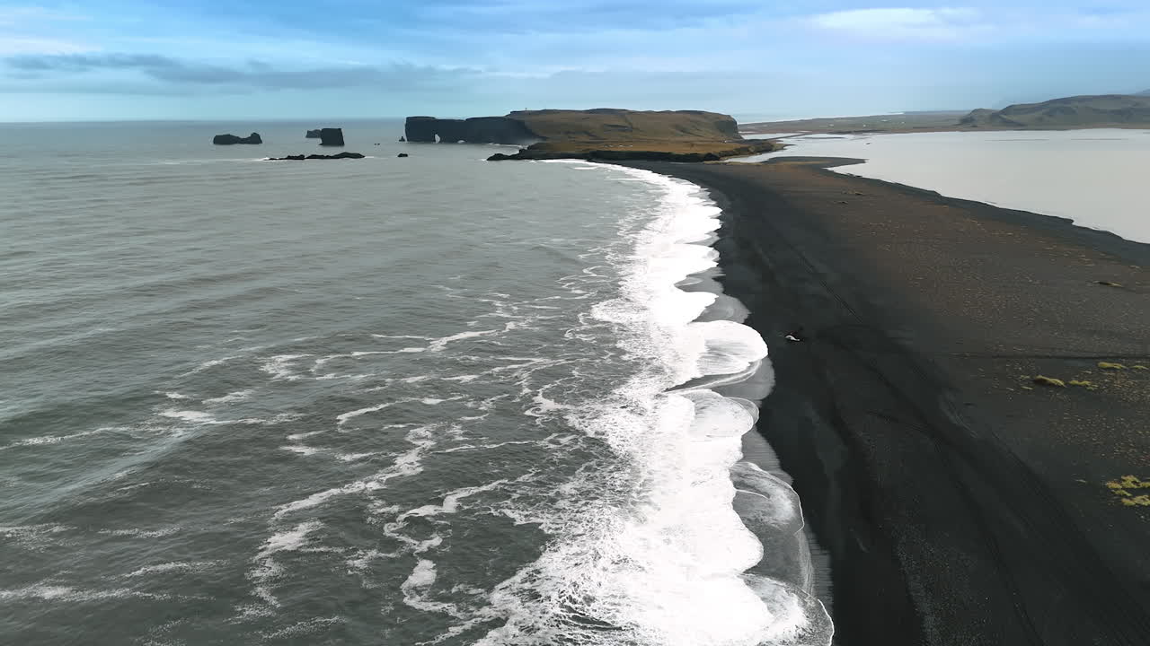 Contrasting white foamy waves with black sandy beach. The North Atlantic Ocean at the coast with volcanic sand. Top view. Iceland scenery.