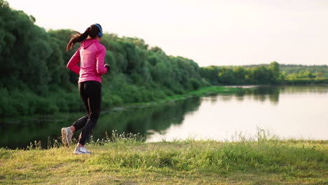 Das-Mädchen-Läuft-Bei-Sonnenuntergang-Im-Park-Am-Teich-Entlang-Und-Hört-Musik-über-Kopfhörer